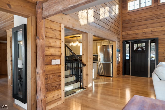 foyer entrance featuring wood walls, a chandelier, light wood-type flooring, a towering ceiling, and log walls