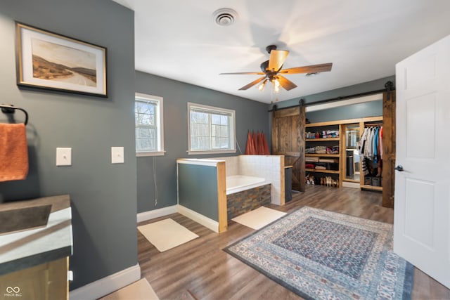 bathroom featuring a relaxing tiled tub, ceiling fan, and hardwood / wood-style flooring