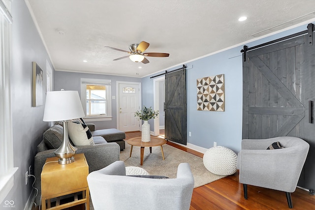 living room with wood-type flooring, ceiling fan, crown molding, a barn door, and a textured ceiling