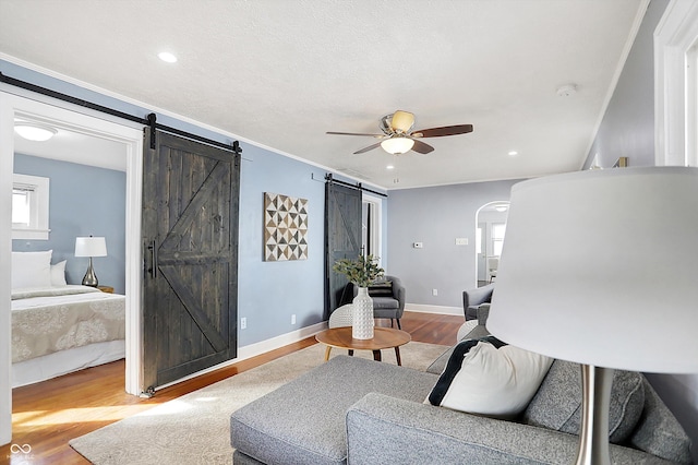 living room featuring crown molding, ceiling fan, a barn door, and light hardwood / wood-style floors