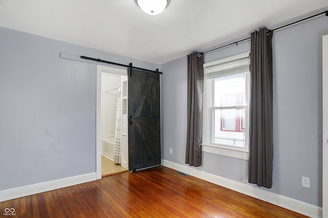 unfurnished bedroom featuring wood-type flooring, a barn door, and ensuite bathroom