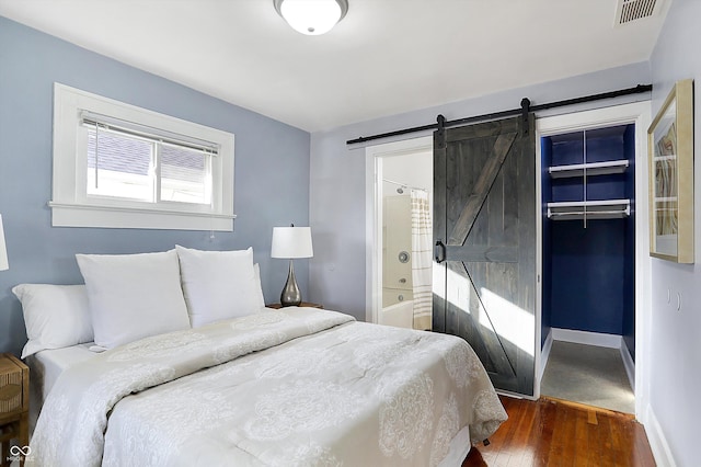 bedroom featuring dark wood-type flooring, ensuite bathroom, a barn door, and a closet