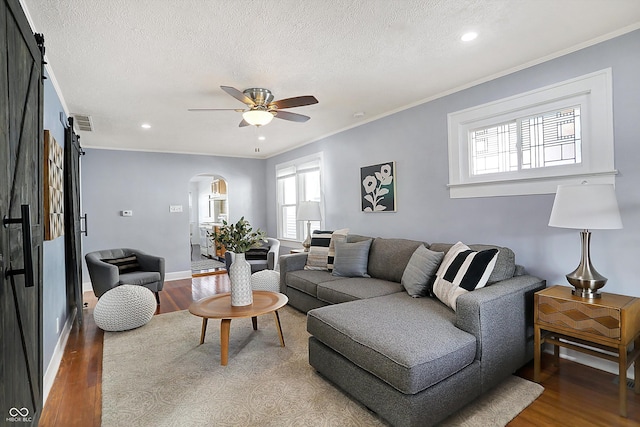 living room featuring hardwood / wood-style flooring, ornamental molding, ceiling fan, a barn door, and a textured ceiling