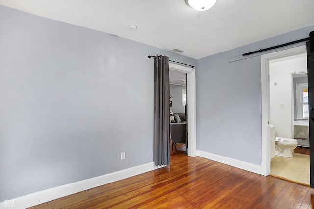 unfurnished bedroom with hardwood / wood-style flooring, connected bathroom, and a barn door