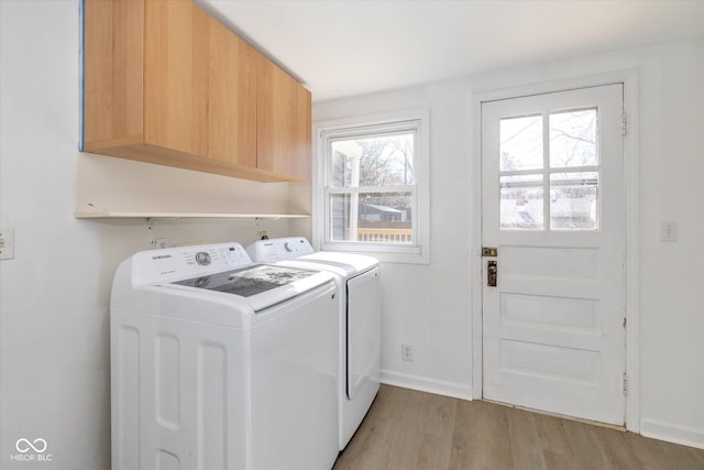 clothes washing area with cabinets, separate washer and dryer, and light wood-type flooring