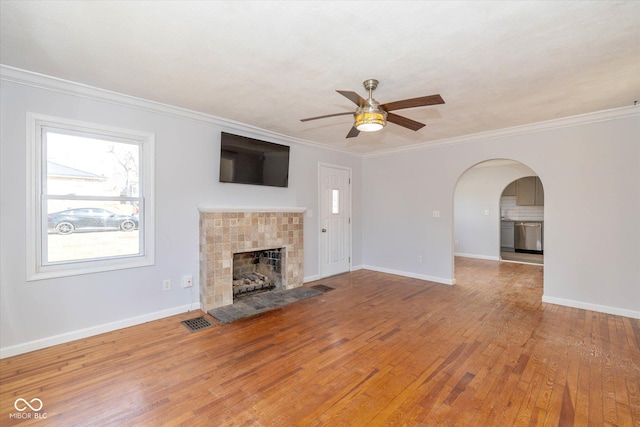 unfurnished living room featuring a tile fireplace, ornamental molding, wood-type flooring, and ceiling fan