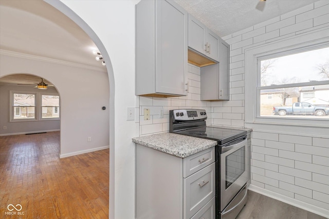 kitchen featuring stainless steel electric stove, light stone countertops, a wealth of natural light, and light wood-type flooring