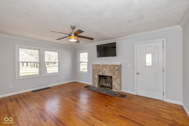 unfurnished living room with crown molding, a textured ceiling, hardwood / wood-style flooring, ceiling fan, and a tiled fireplace