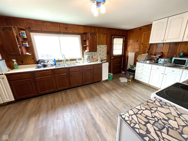 kitchen with white cabinetry, sink, light hardwood / wood-style floors, and wood walls