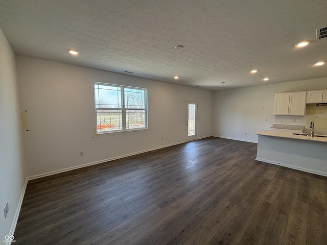 unfurnished living room featuring dark wood finished floors, recessed lighting, a textured ceiling, and baseboards