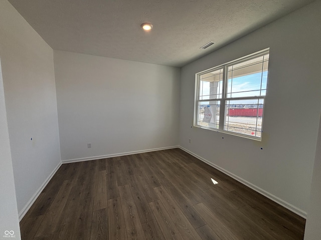 empty room featuring visible vents, baseboards, a textured ceiling, and dark wood-style flooring