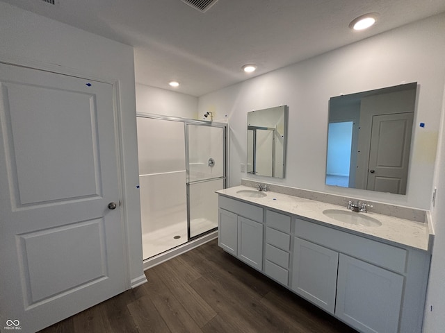 bathroom featuring double vanity, a shower stall, wood finished floors, and a sink