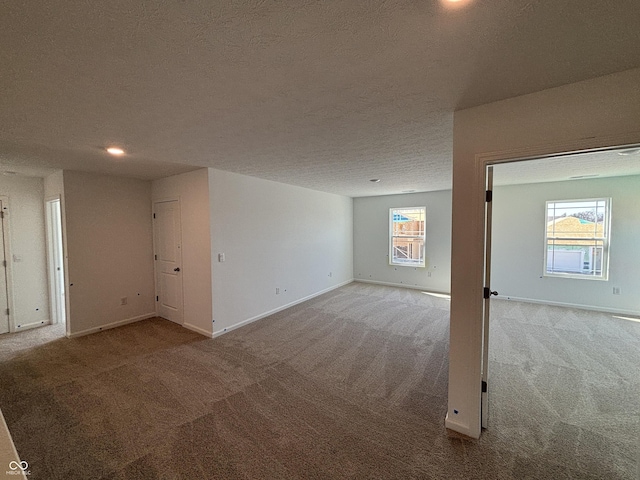 carpeted empty room with baseboards, a wealth of natural light, and a textured ceiling