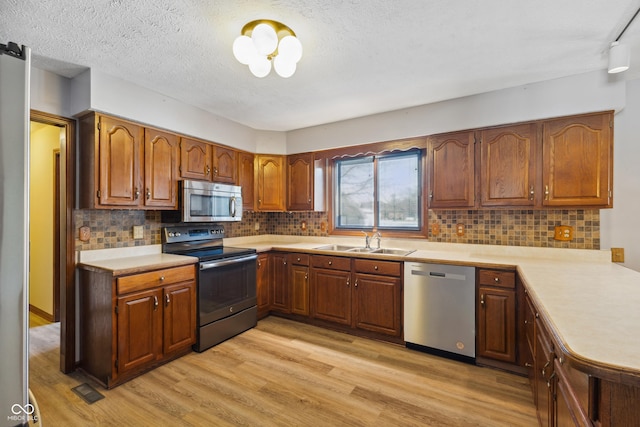 kitchen with stainless steel appliances, sink, light hardwood / wood-style floors, and decorative backsplash