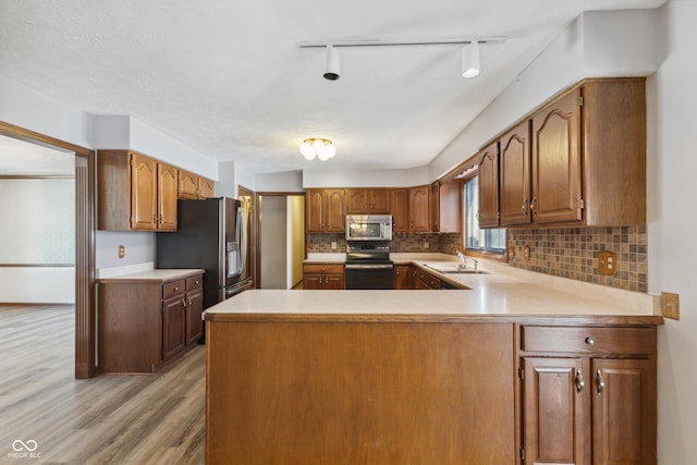 kitchen with sink, tasteful backsplash, light wood-type flooring, kitchen peninsula, and stainless steel appliances