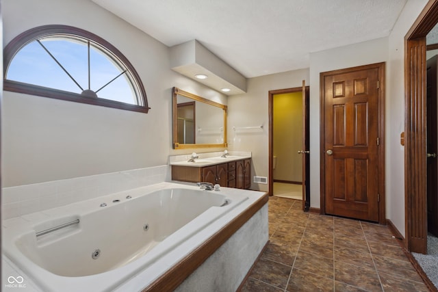 bathroom with vanity, tiled tub, and a textured ceiling