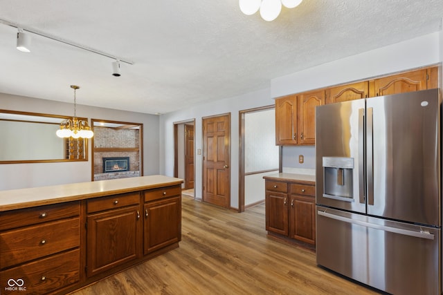 kitchen with a fireplace, decorative light fixtures, stainless steel fridge, a textured ceiling, and light hardwood / wood-style flooring