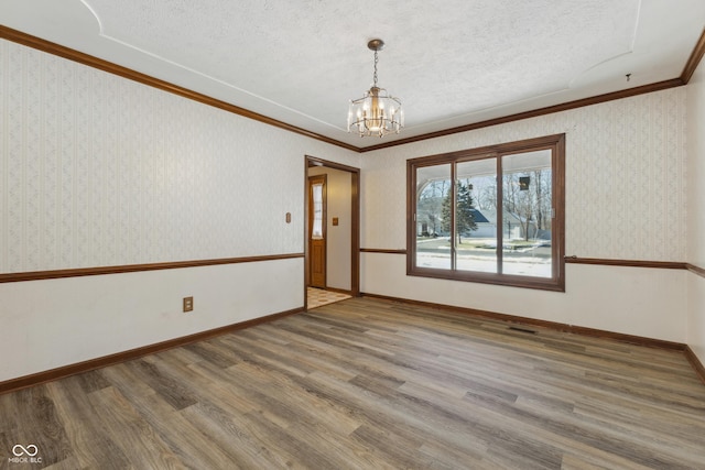 empty room with hardwood / wood-style flooring, crown molding, a textured ceiling, and a chandelier