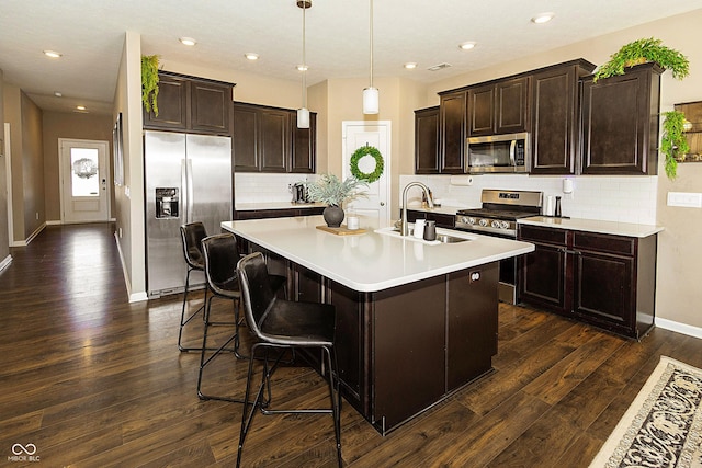 kitchen with sink, dark hardwood / wood-style flooring, an island with sink, pendant lighting, and stainless steel appliances