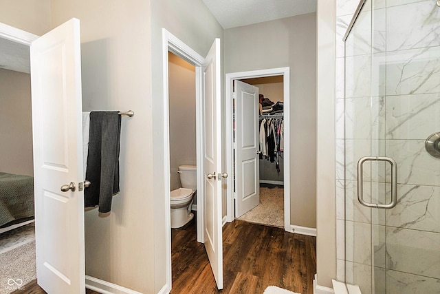 bathroom with wood-type flooring, a shower with door, and toilet