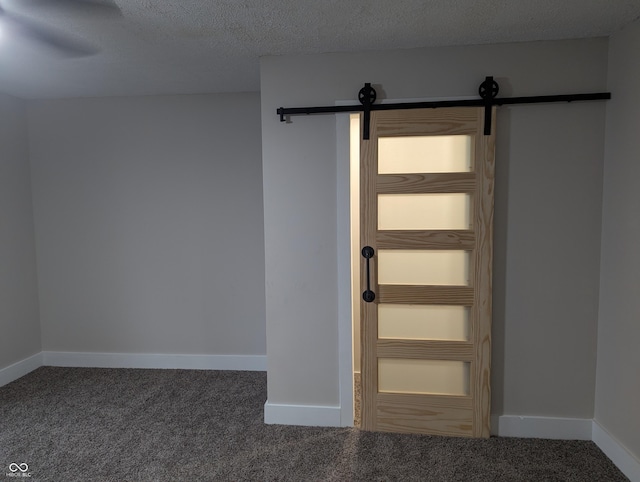 interior space featuring dark carpet, a barn door, and a textured ceiling