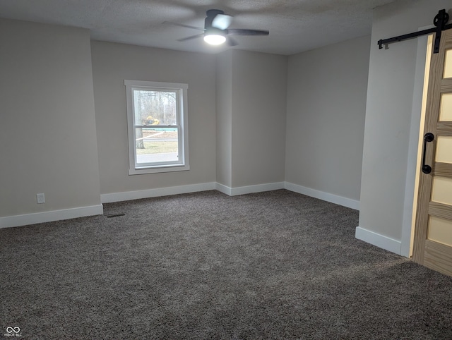 carpeted empty room featuring ceiling fan, a barn door, and a textured ceiling