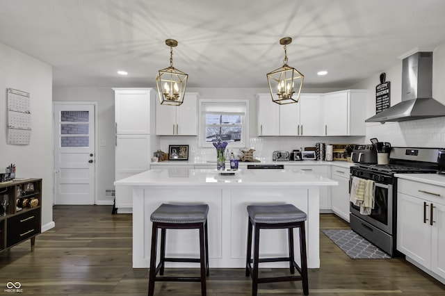 kitchen featuring white cabinetry, decorative light fixtures, stainless steel gas stove, and wall chimney exhaust hood