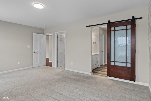 unfurnished bedroom with ensuite bathroom, a barn door, and light carpet