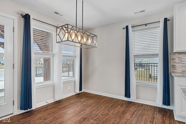 unfurnished dining area featuring plenty of natural light, a notable chandelier, and dark hardwood / wood-style flooring