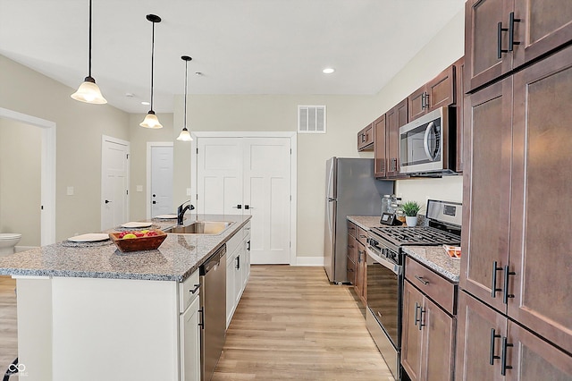 kitchen with sink, white cabinetry, hanging light fixtures, appliances with stainless steel finishes, and light stone countertops