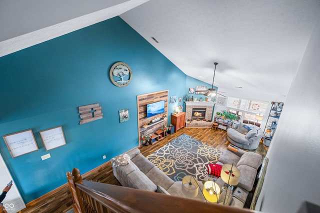 living room with hardwood / wood-style flooring, ceiling fan, high vaulted ceiling, and a brick fireplace