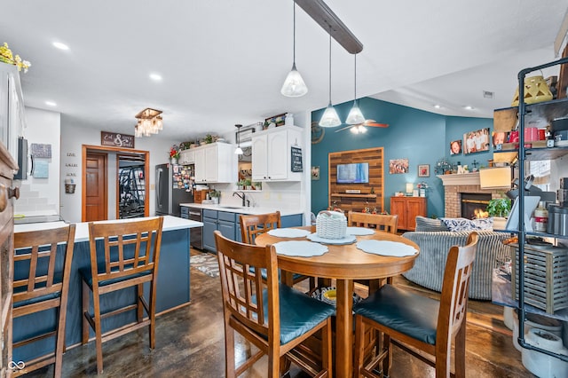 dining area featuring vaulted ceiling, ceiling fan, a fireplace, and sink