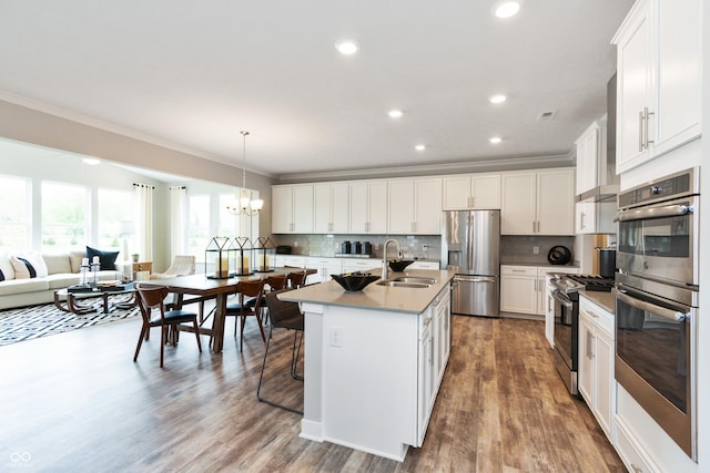 kitchen with appliances with stainless steel finishes, white cabinetry, sink, hanging light fixtures, and a kitchen island with sink