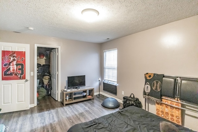 bedroom with wood-type flooring, a walk in closet, and a textured ceiling