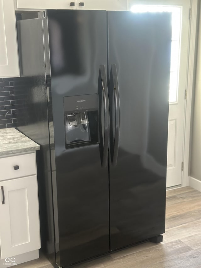 kitchen featuring black fridge, light hardwood / wood-style floors, tasteful backsplash, and white cabinets