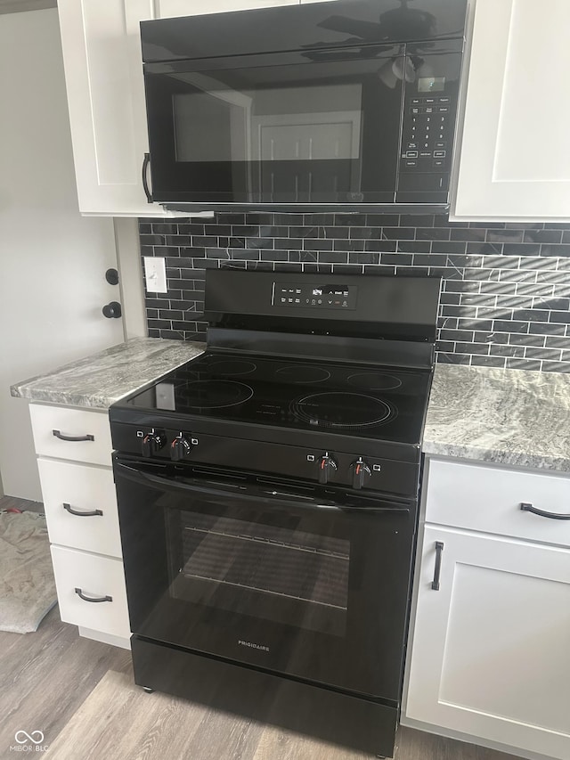 kitchen featuring light stone counters, white cabinets, light hardwood / wood-style floors, and black appliances