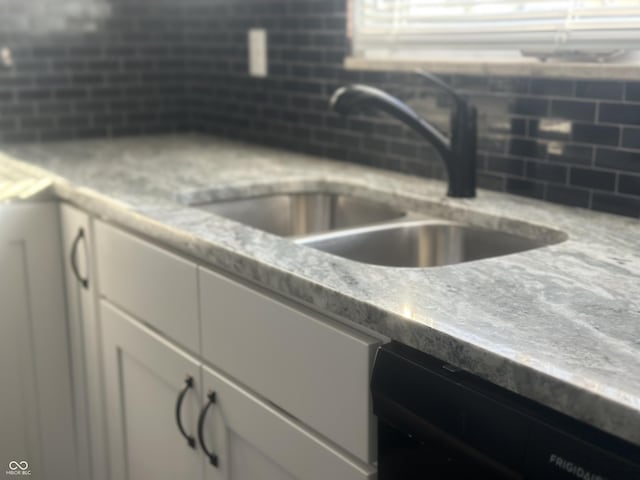 room details with tasteful backsplash, sink, black dishwasher, and white cabinets