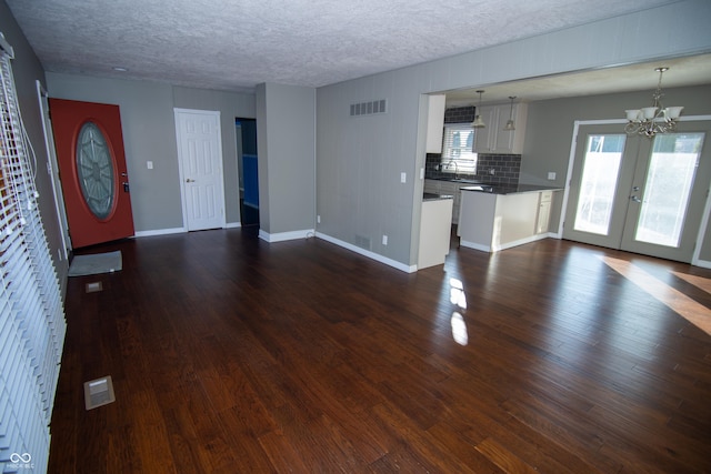 unfurnished living room with a chandelier, a textured ceiling, dark hardwood / wood-style flooring, and french doors