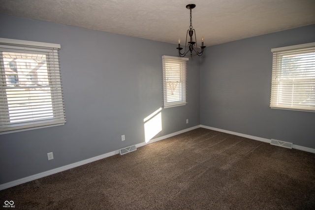 empty room with an inviting chandelier, a healthy amount of sunlight, carpet floors, and a textured ceiling