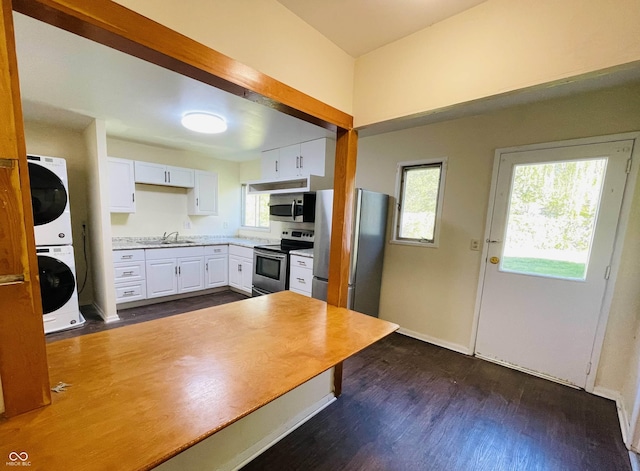 kitchen featuring dark hardwood / wood-style floors, stainless steel appliances, stacked washing maching and dryer, and white cabinets