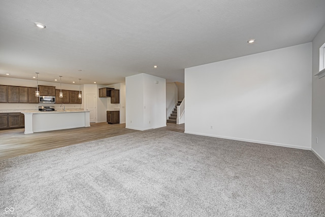 unfurnished living room with recessed lighting, stairs, a sink, and light colored carpet