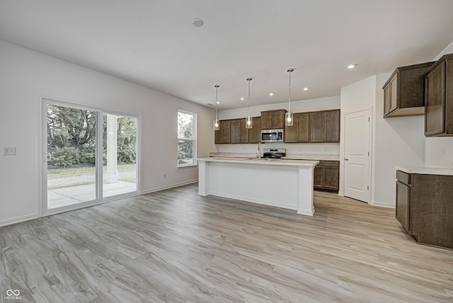 kitchen featuring decorative light fixtures, light wood finished floors, stainless steel appliances, light countertops, and a kitchen island with sink