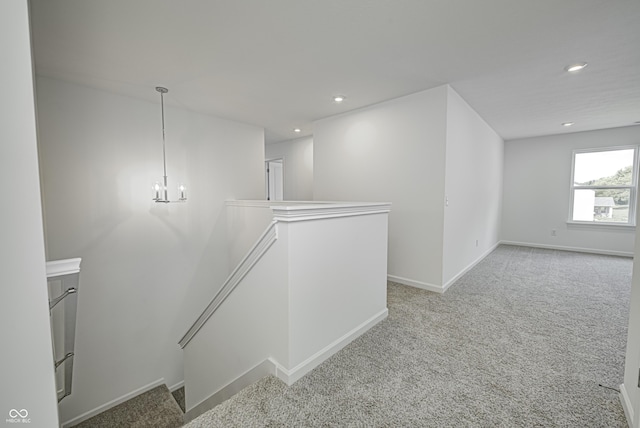 hall with baseboards, light colored carpet, a notable chandelier, and an upstairs landing