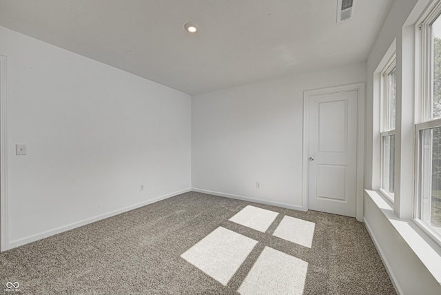 unfurnished room with a wealth of natural light, dark carpet, visible vents, and baseboards