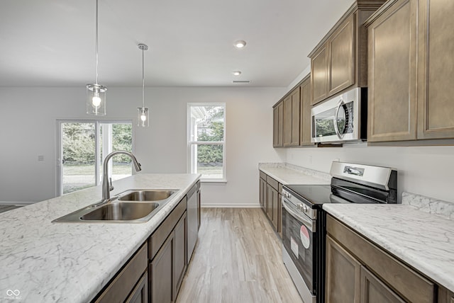 kitchen with appliances with stainless steel finishes, light wood-style floors, a sink, and light stone counters