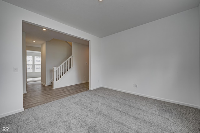 empty room with dark carpet, stairway, and baseboards