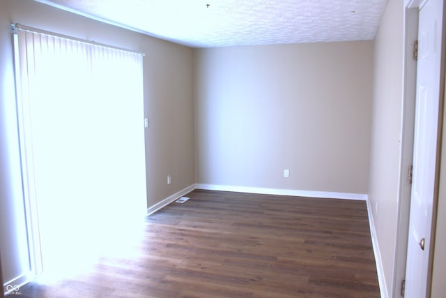 empty room with dark wood-type flooring and a textured ceiling