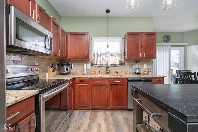 kitchen featuring sink, tasteful backsplash, hanging light fixtures, light hardwood / wood-style flooring, and appliances with stainless steel finishes