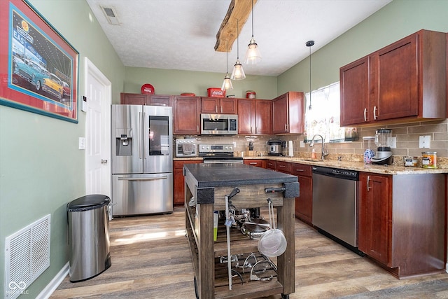 kitchen featuring tasteful backsplash, sink, hanging light fixtures, stainless steel appliances, and light wood-type flooring