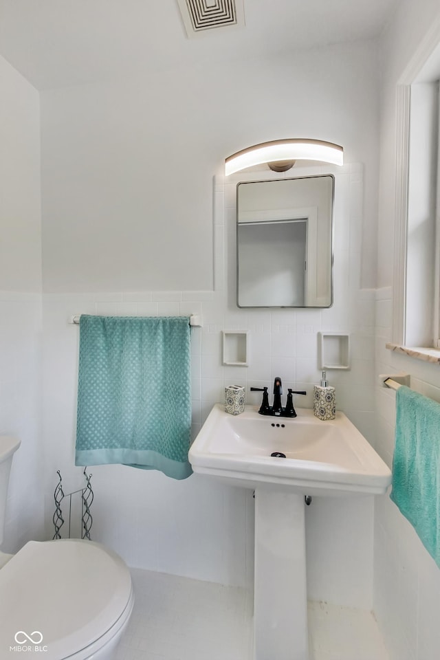 bathroom featuring toilet, sink, and tile walls